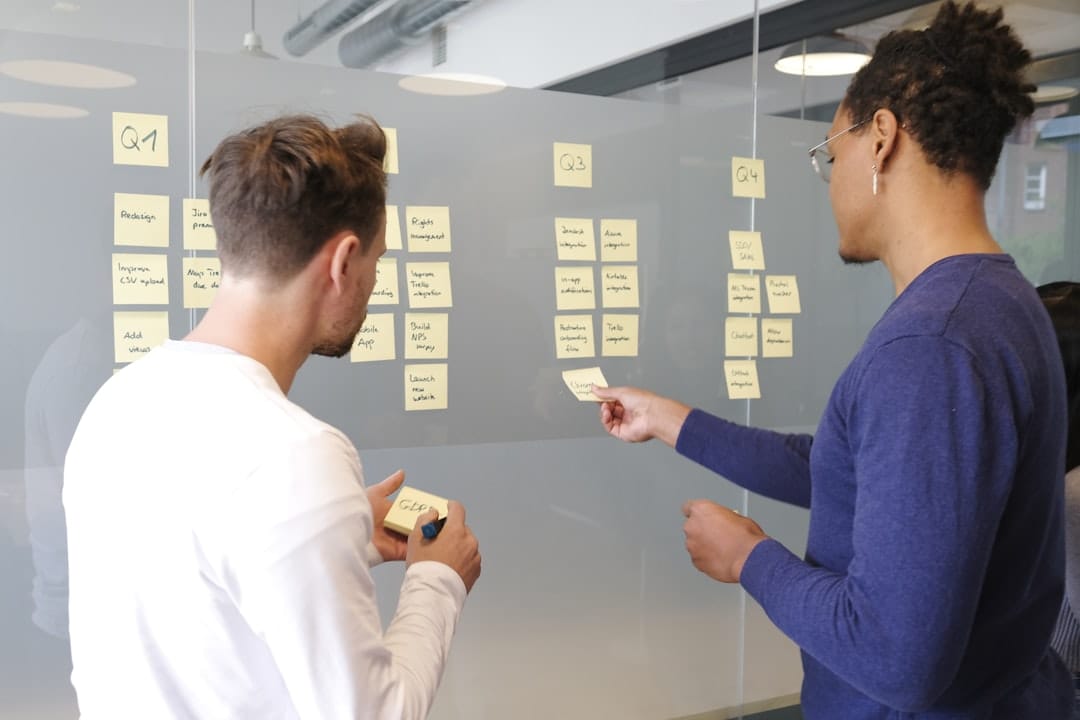 Two people collaborating on a project plan using yellow sticky notes on a glass wall